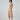 Woman wearing a ribbed cream midi dress with a minimalist design, standing in Australia. The dress falls just below the knee and fits closely to her body, accentuating her figure. She accessorizes with simple jewelry and wears her hair in a sleek and understated style