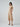 Woman wearing a ribbed cream midi dress with a minimalist design, standing in Australia. The dress falls just below the knee and fits closely to her body, accentuating her figure. She accessorizes with simple jewelry and wears her hair in a sleek and understated style